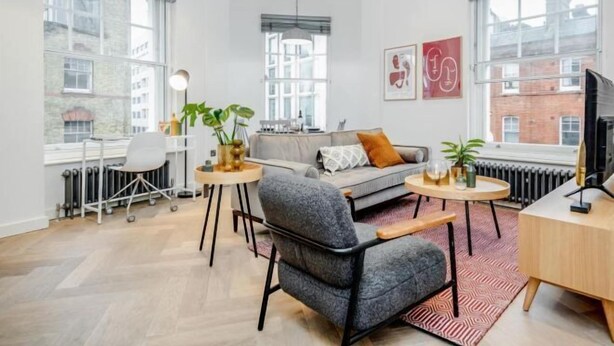 A modern living room with a grey sofa, a small round table, a chair, and a TV. - Kula London - Fitzrovia Newman St (London)