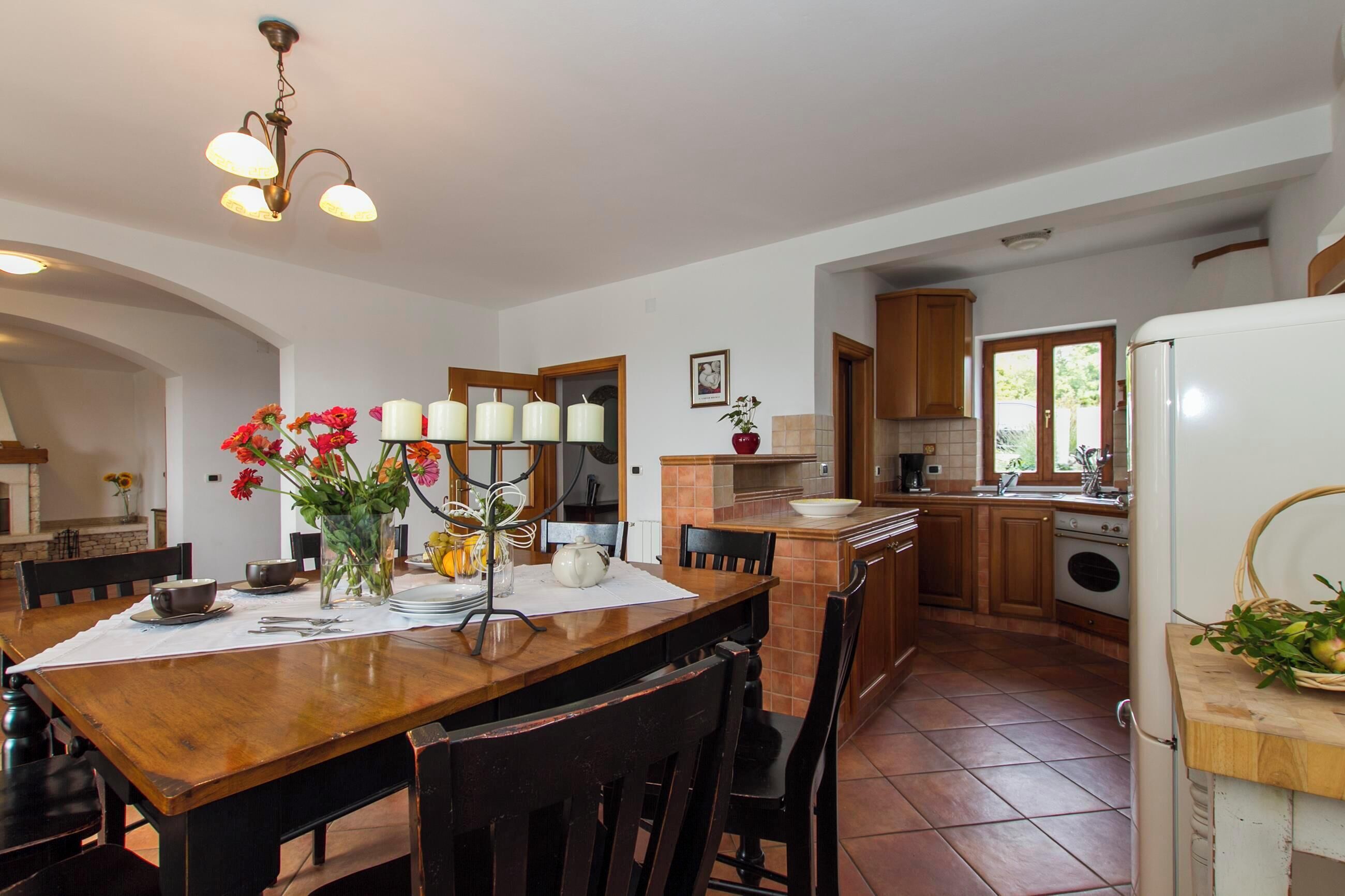 A kitchen with a wooden table, chairs, a chandelier, and a refrigerator.