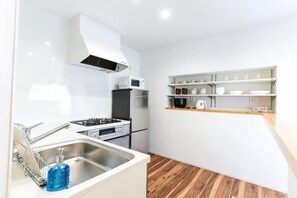 A compact kitchen with a gas stove, a sink, and a microwave. - Mirai Stay Yokote (Kumamoto)