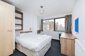 Una camera d'albergo con un letto, una scrivania, un armadio e una finestra vista città.