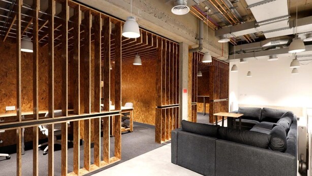 A modern office space with exposed wooden beams, a grey sofa, and pendant lighting. - Student Only AXO Camden (London)