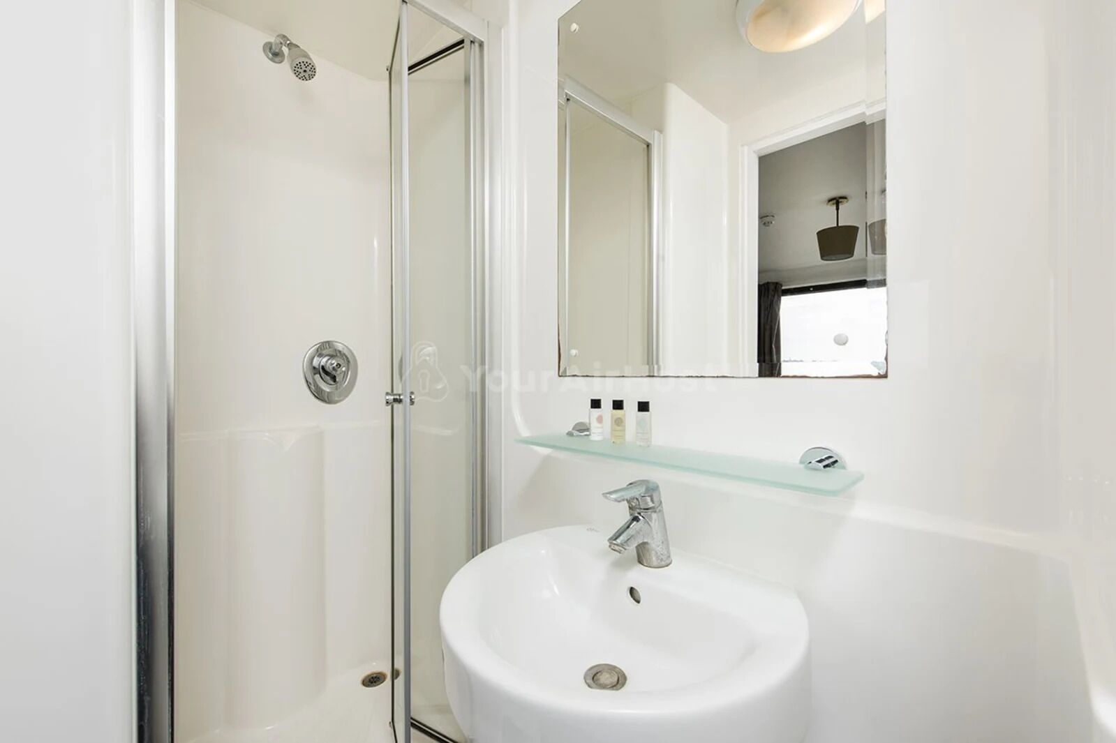 A modern bathroom with a glass shower enclosure, a white sink, and a mirror above the sink.
