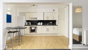 A modern kitchen with white cabinets, a black countertop, and stainless steel appliances. There is a small dining area with a table and two chairs. - Student Only AXO Camden (London)