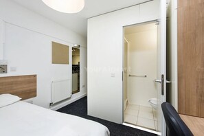 Camera d'albergo con un letto, una testiera in legno, un termosifone, uno specchio e un angolo doccia.