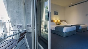 A hotel room with a balcony, a bed with two pillows, a bedside table with a lamp, and a window. - Hotel Cavalier (Beirut)
