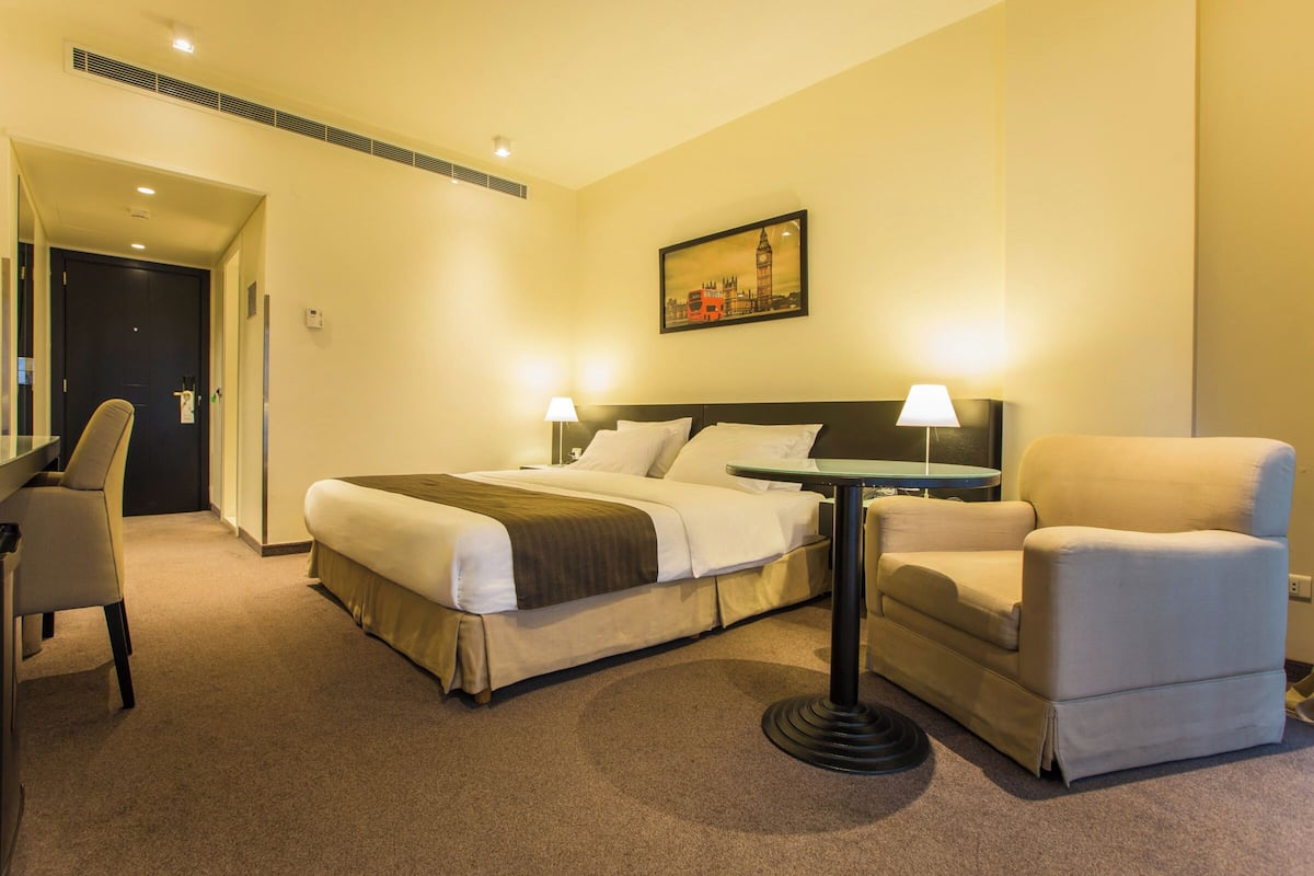 A hotel room with a bed, a desk, a chair, and a table.
