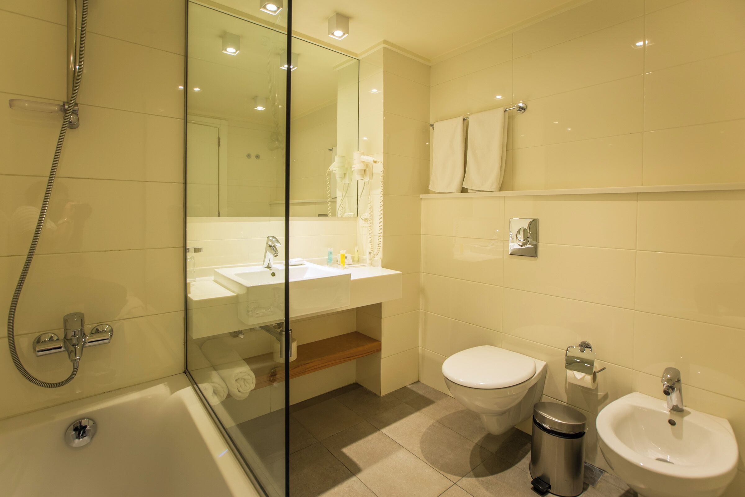 A modern bathroom with a glass-enclosed shower, a sink, a toilet, and a bidet.