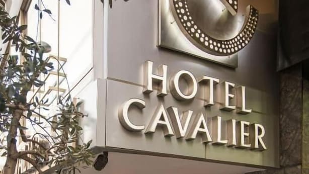 The exterior of Hotel Cavalier with a prominent sign, a covered entrance, and potted plants along the walkway. - Hotel Cavalier (Beirut)