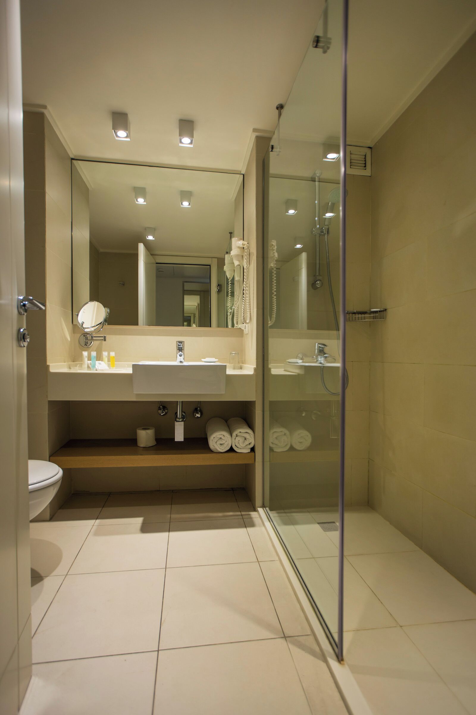 A modern bathroom with a glass-enclosed shower, a large mirror, and a sink with toiletries.