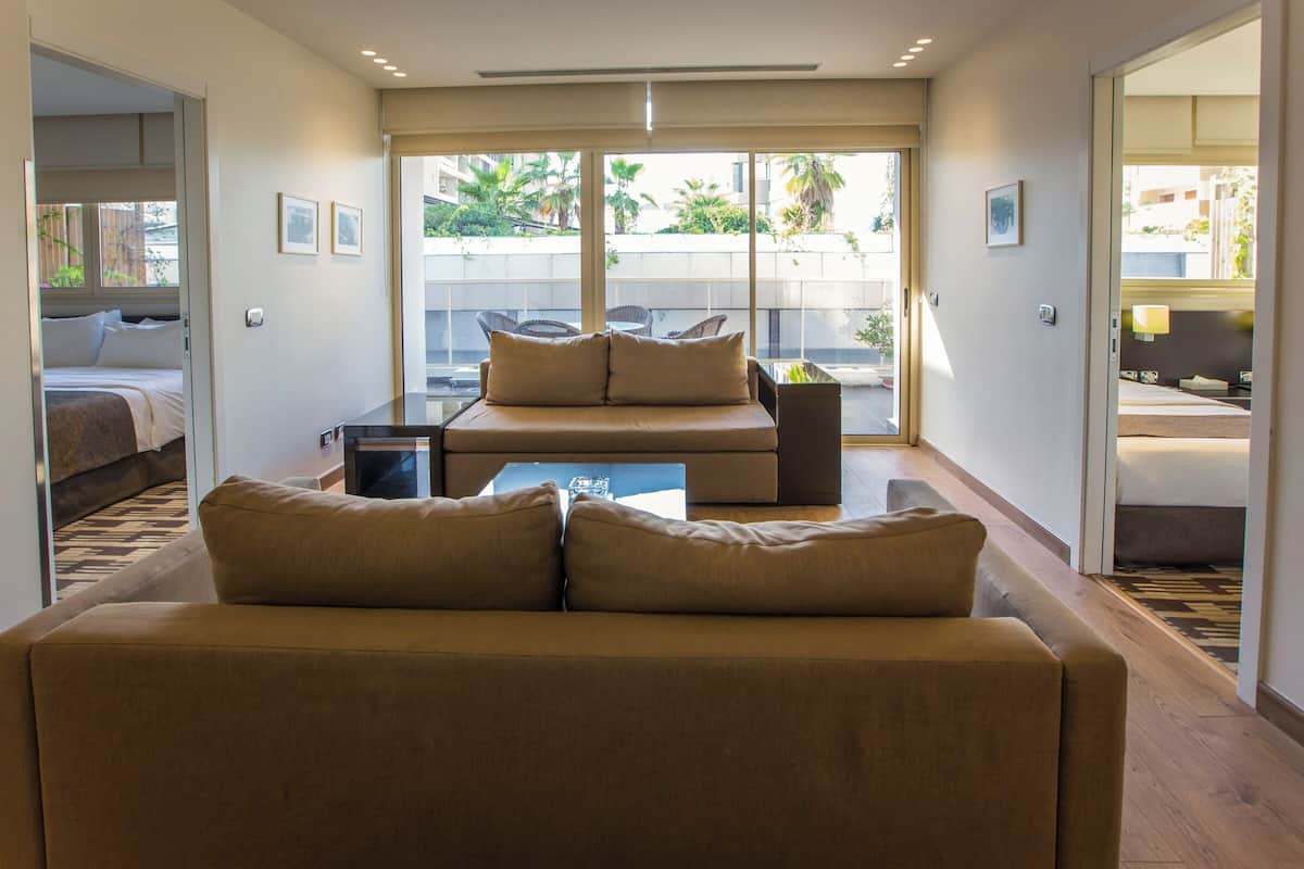 A modern living room with a sofa, a coffee table, and a view of a courtyard through large sliding glass doors.