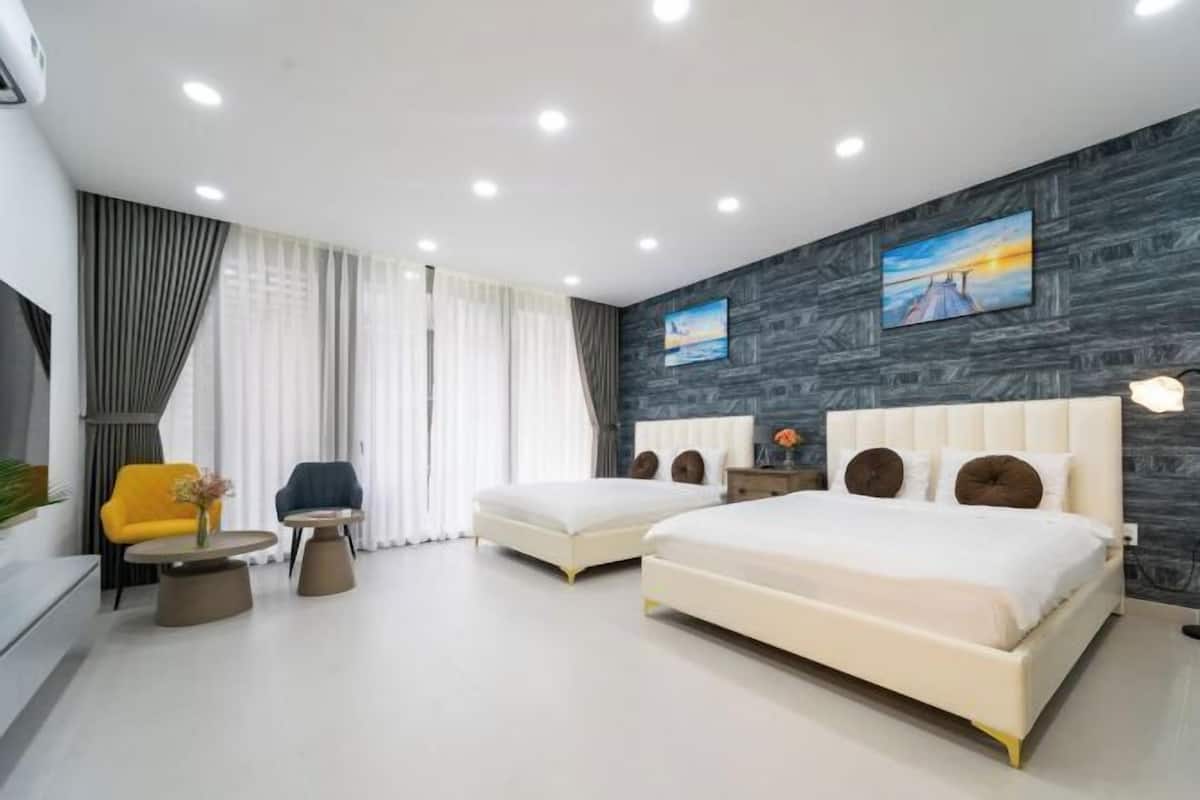 Une chambre d’hôtel moderne avec deux lits, un canapé, une petite table et une grande fenêtre avec des rideaux.