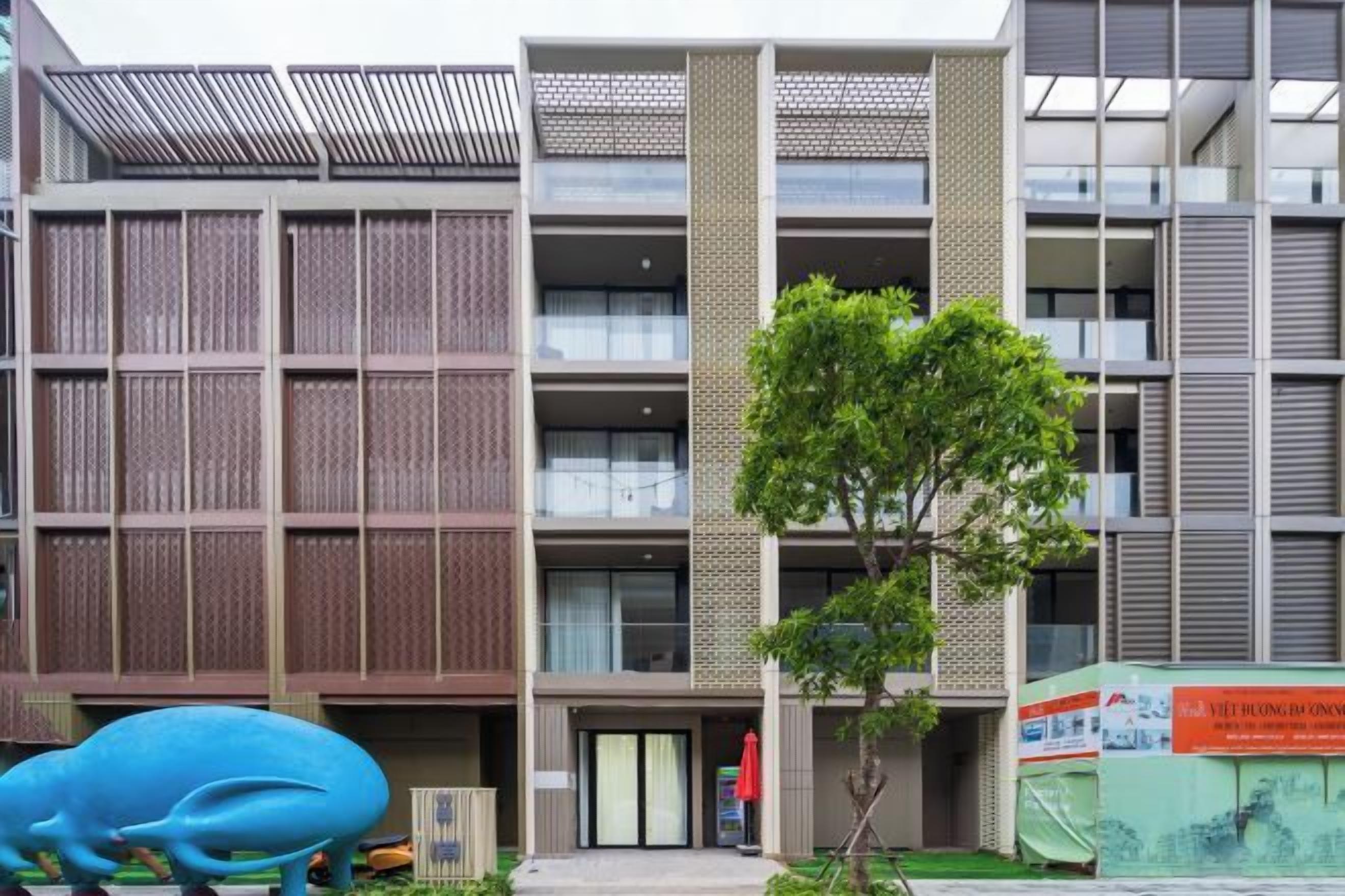 Un edificio moderno con un ingresso centrale, diversi piani e un albero di fronte.