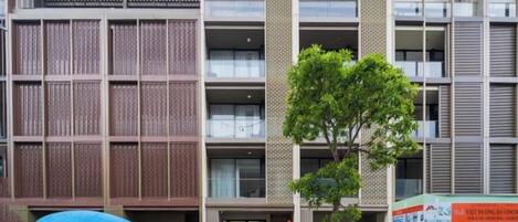 A modern building with a central entrance, multiple floors, and a tree in front.