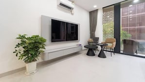 Un salon moderne avec un téléviseur à écran plat fixé au mur, une plante en pot, une table basse ronde et un canapé.