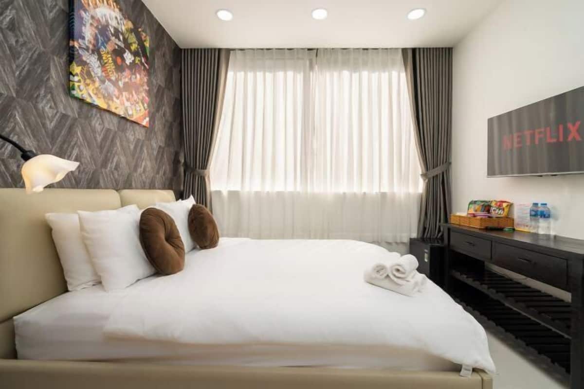 Une chambre d’hôtel avec un lit, une télévision, un bureau et une fenêtre avec des rideaux.