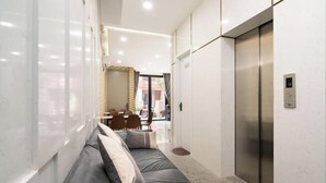 Un couloir d’hôtel moderne avec un canapé, un ascenseur et un coin repas en arrière-plan.