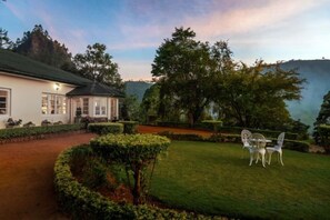 A house with a well-maintained lawn, a patio with chairs, and a view of the surrounding landscape. - Highgrove Estate By Ishq (Nuwara Eliya District)