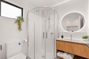 Un baño moderno con cabina de ducha de vidrio, tocador de madera, espejo redondo y radiador.