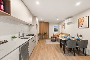 A modern kitchen with a built-in dishwasher, a dining area with a table and chairs, and a view through the window.
