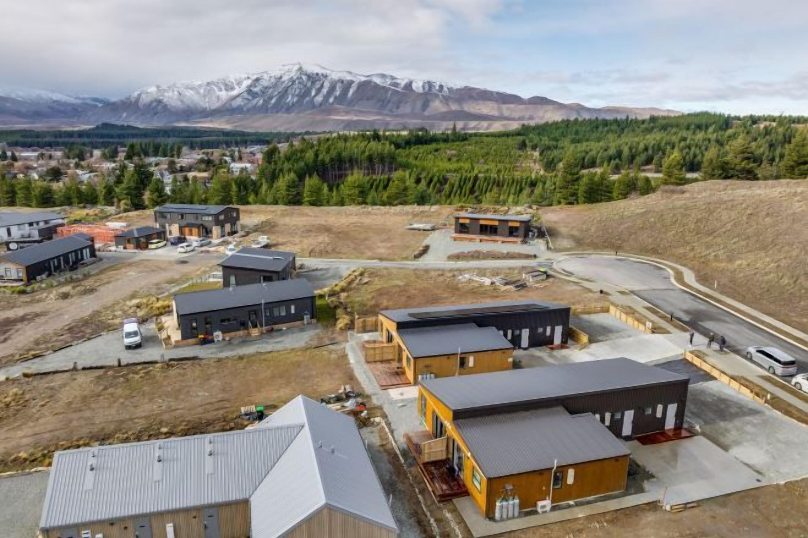 An aerial view of a commercial area with buildings, a parking lot, and a mountainous backdrop.