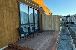A wooden exterior with large windows, a deck with chairs, and a gravel path. - Starlet 11 (Lake Tekapo)