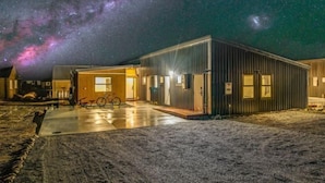 A modern building with a metal exterior and a wooden door, set against a starry night sky. - Starlet 11 (Lake Tekapo)