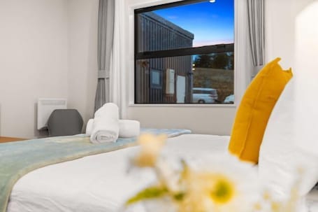 A hotel room with a bed, a window with a view of a building, a desk, and a chair.
