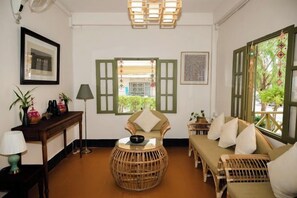 A room with a sofa, a round wicker table, a lamp, and a window with green shutters. - Barn Laos Luangprabang Heritage (Luang Prabang)