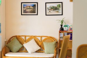 Un canapé en osier avec des coussins, un tableau encadré accroché au mur et une petite table sur laquelle sont posés divers objets.