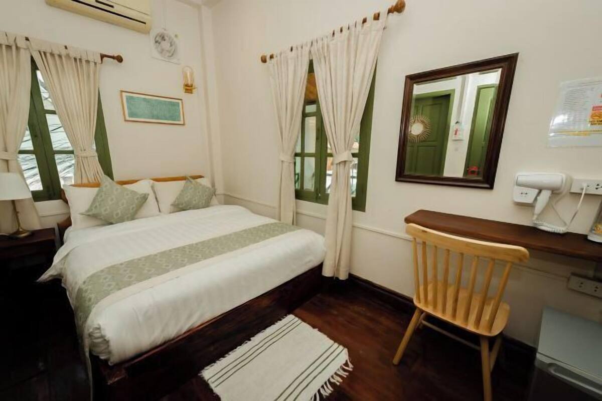A bedroom with a bed, a wooden chair, a desk, and a mirror.