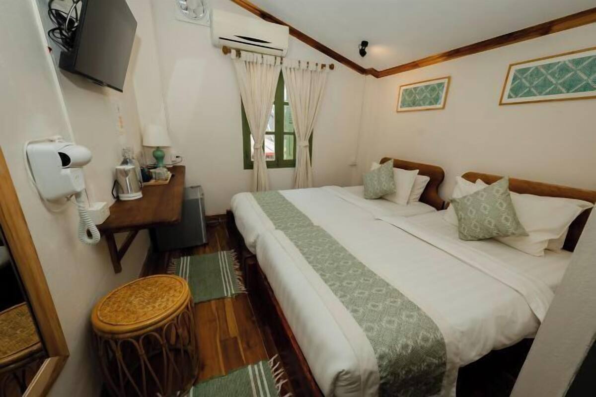 A hotel room with a bed, a desk, a chair, an air conditioner, a mirror, and a window with curtains.