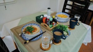 Una mesa de comedor con un tazón de fideos, palillos, un vaso de agua y aderezos.