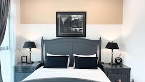 Une chambre à coucher bien rangée, avec un lit placé au centre, entre deux tables de chevet, chacune surmontée d’une lampe. Un tableau encadré est accroché au-dessus du lit.