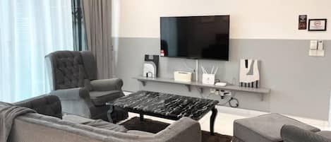 A modern living room with a sofa, armchairs, a coffee table, a flat-screen TV, and a mounted air conditioner.