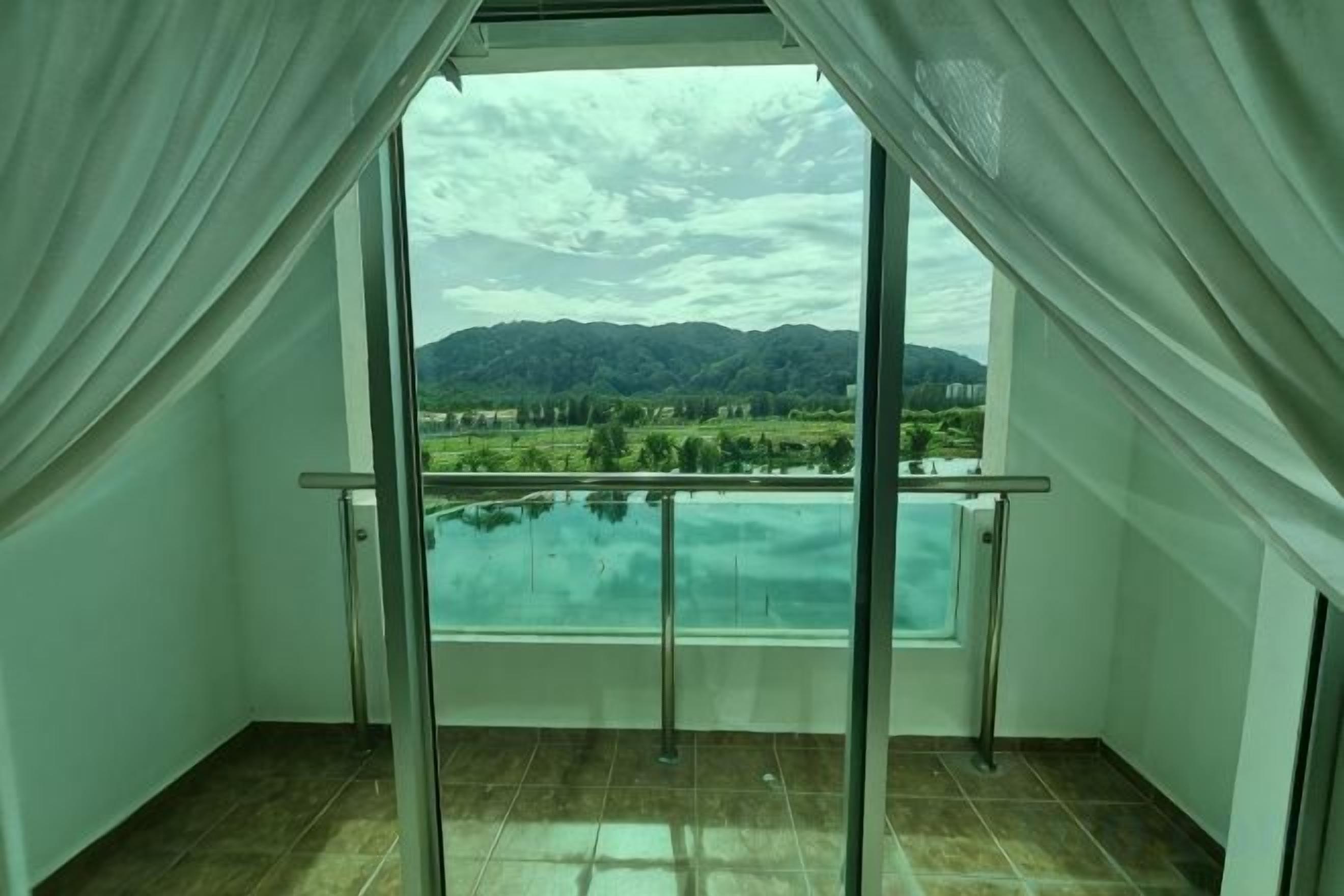 A balcony with a glass door and curtains, offering a view of a mountainous landscape and a body of water.