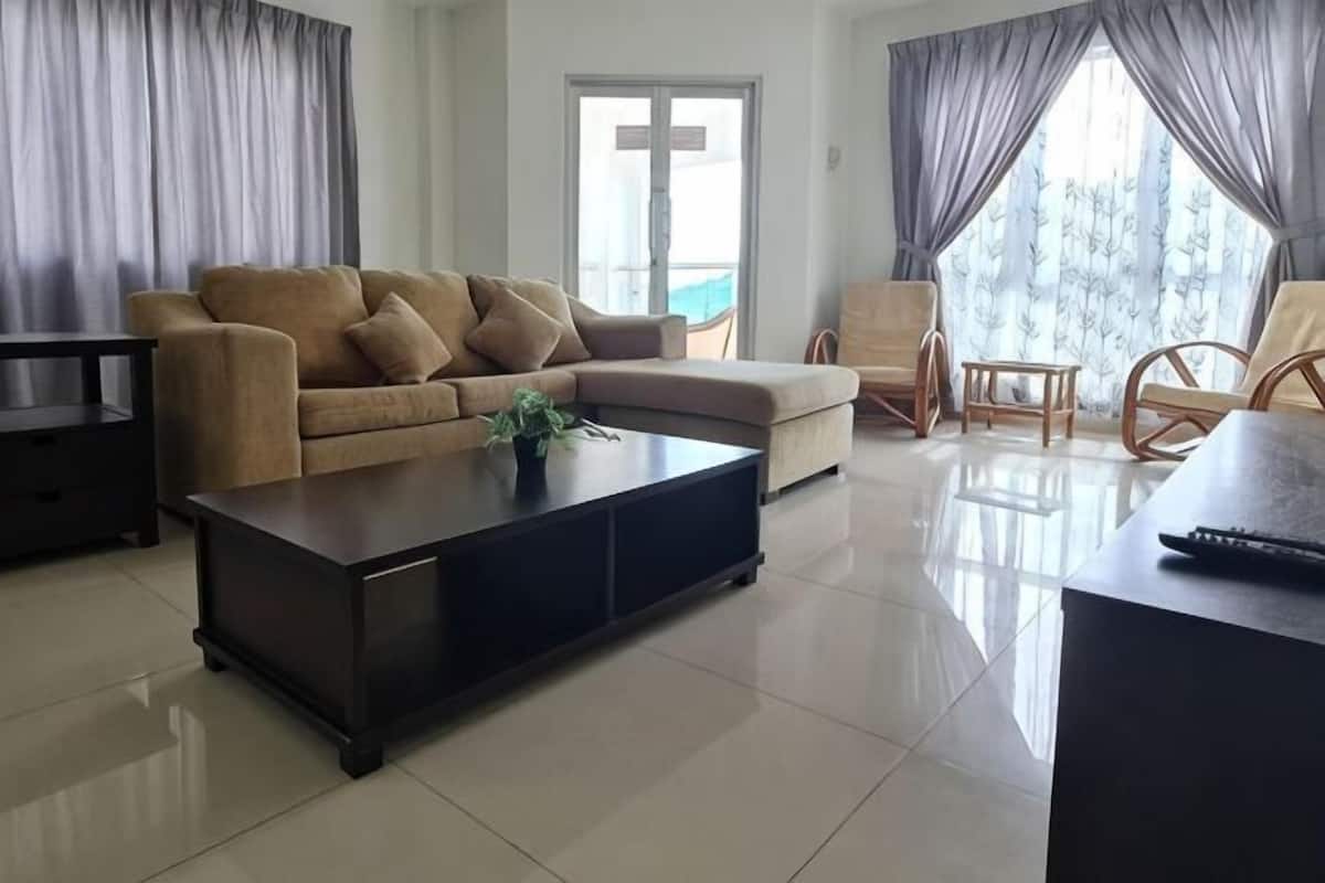 A living room with a sofa, a coffee table, a TV, and a window with curtains.