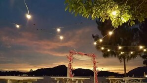 Ambiente à beira do lago com luzes de corda, arco floral e mesas de piquenique.