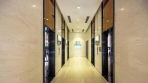 Ein moderner Hotelkorridor mit Marmorwänden, schwarzen Aufzugtüren und Holzboden.