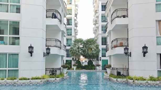 Un hotel moderno con piscina central, varios balcones y abundante vegetación.