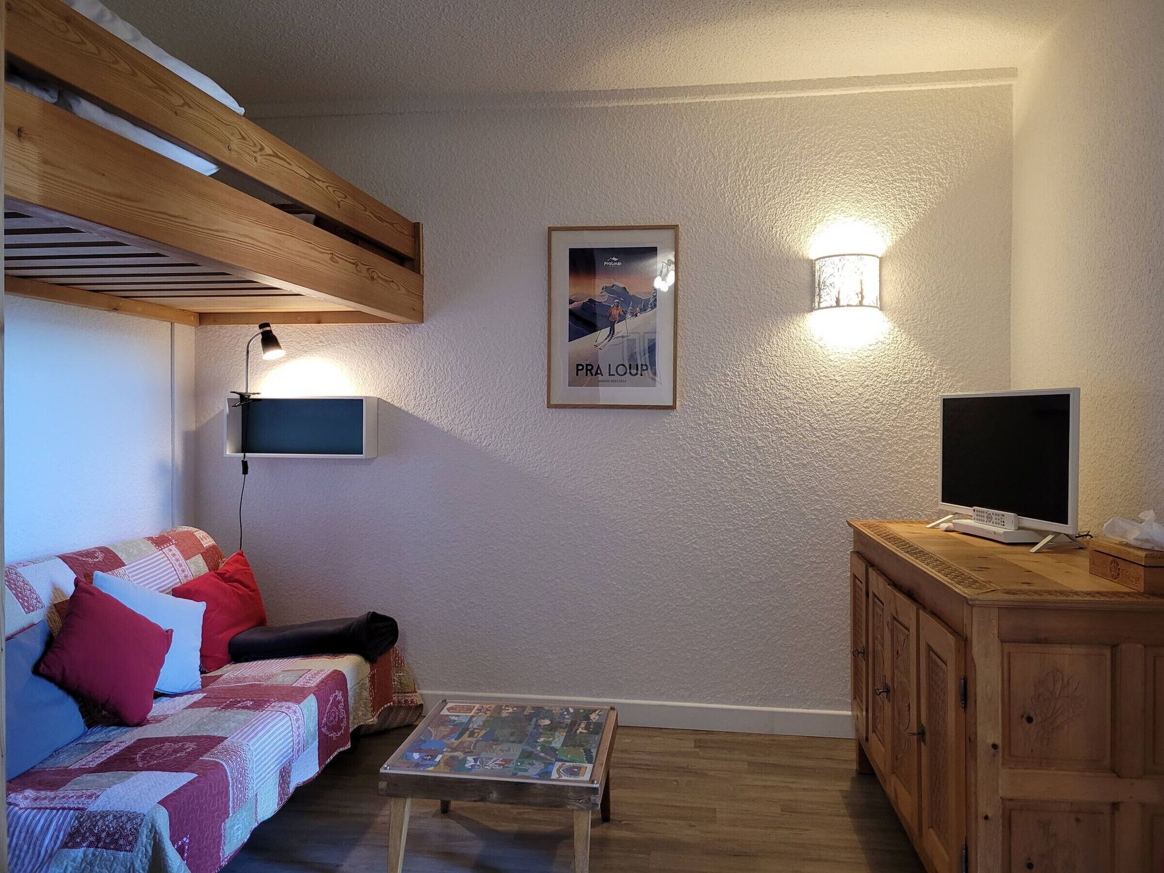 Tunnelmallinen olohuone, jossa on puinen katto, värikkäillä tyynyillä varustettu sohva, pieni sohvapöytä, televisio ja kaappi.