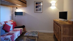 Un salon chaleureux avec un plafond en bois, un canapé agrémenté de coussins colorés, une petite table basse, un téléviseur et un meuble.
