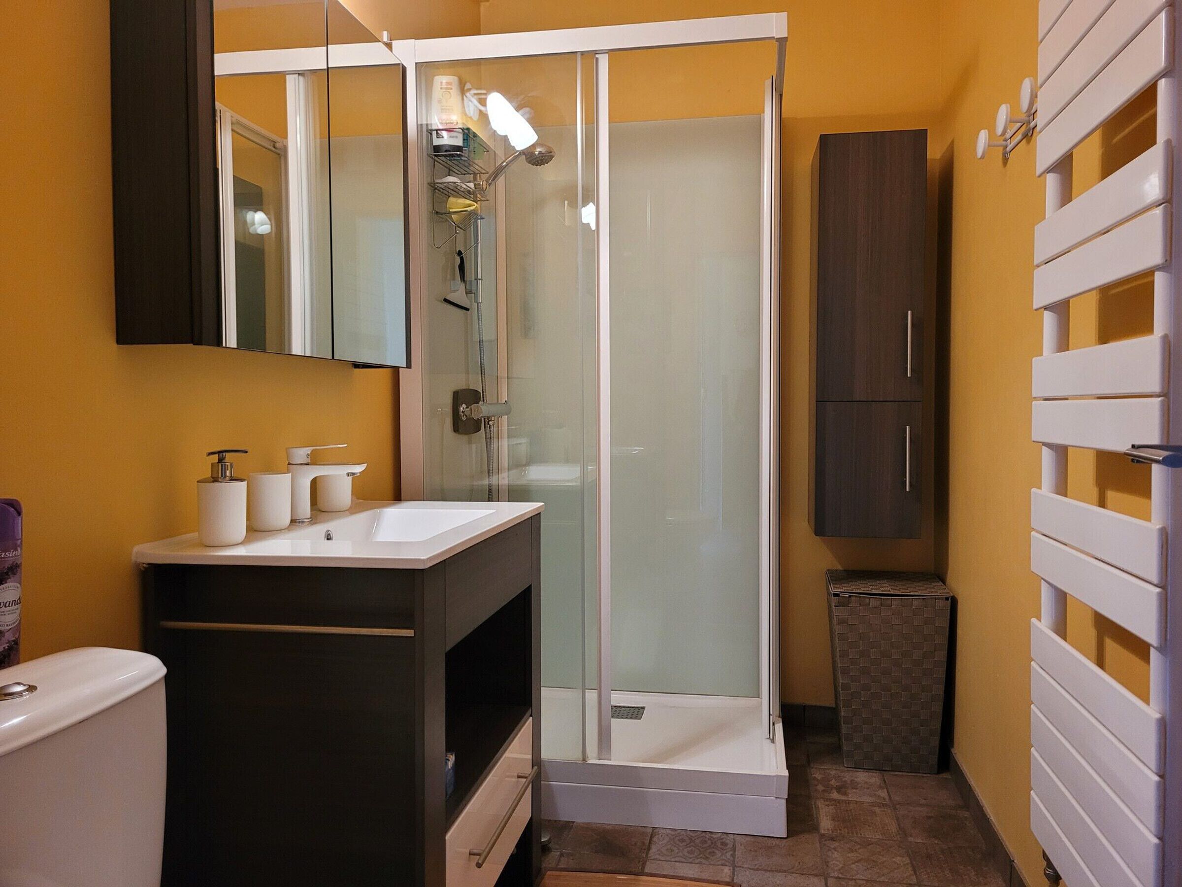 A bathroom with a glass-enclosed shower, a white sink, a dark cabinet, and a mirror above the sink.