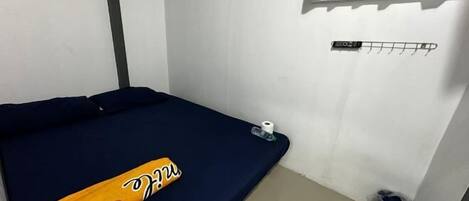Habitació petita amb un llit, una finestra amb cortines, aire condicionat fixat a la paret, una tovallola i un safata de brossa.