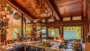 Une cuisine rustique avec des poutres en bois, une vue sur un lac, ainsi que divers ustensiles de cuisine et casseroles.