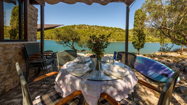 Un espace de restauration en plein air avec une table dressée pour deux personnes, offrant une vue sur un lac et entouré d’arbres.
