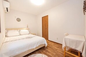 A bedroom with a bed, bedside table, and a small table with a tablecloth. - W.Hostel (Tokyo)