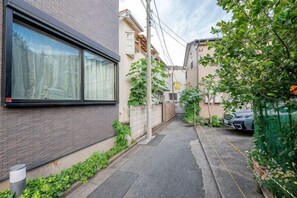 A narrow urban alley with a building on the left, a parked car on the right, and a tree in the foreground. - W.Hostel (Tokyo)