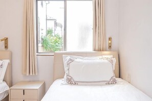 A hotel room with a bed, a bedside table, a nightstand, and a window with curtains. - W.Hostel (Tokyo)