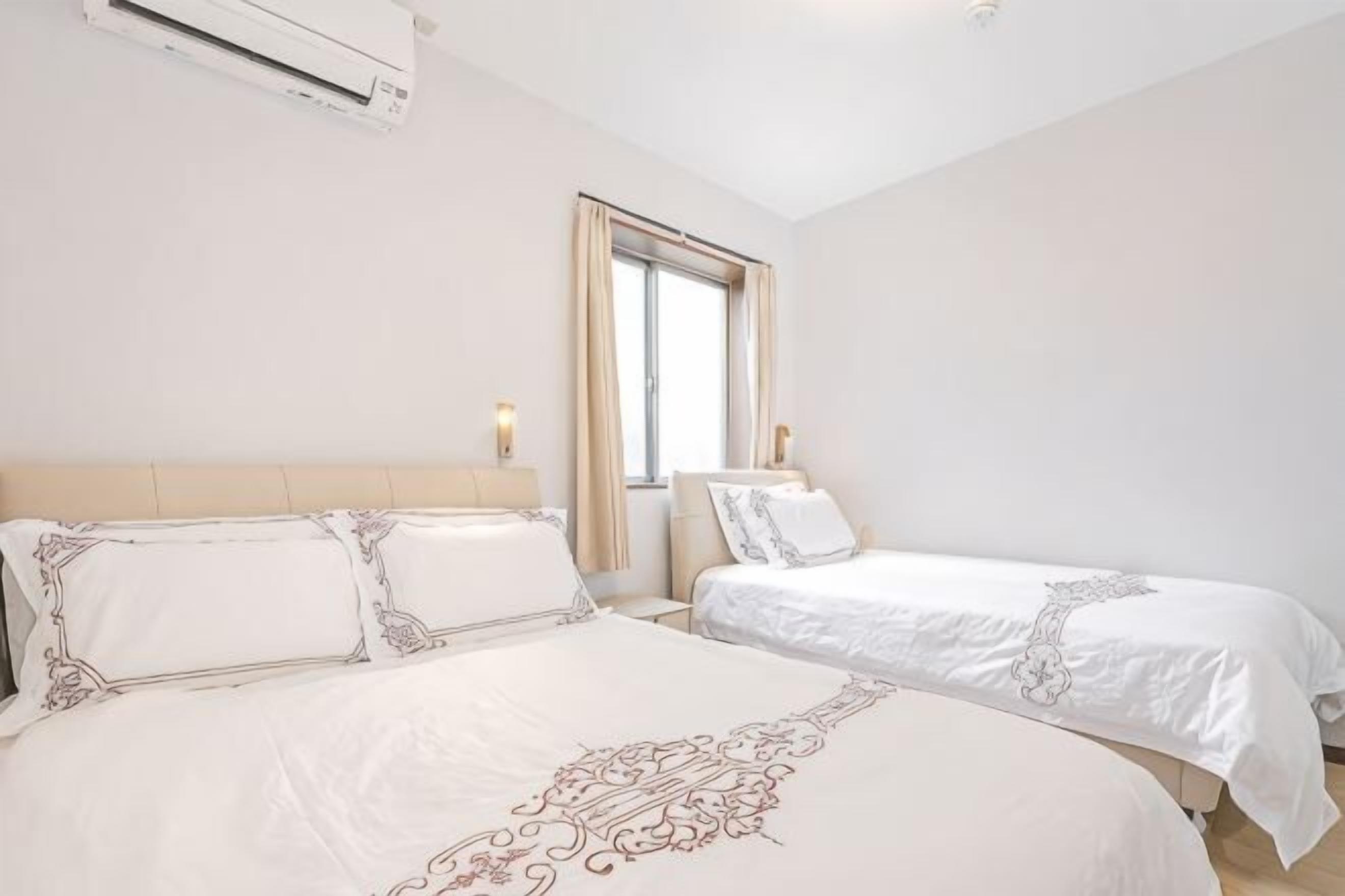 A hotel room with two beds, a window, and an air conditioning unit.