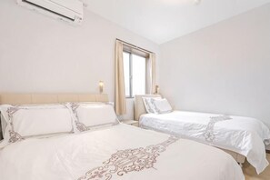 A hotel room with two beds, a window, and an air conditioning unit.